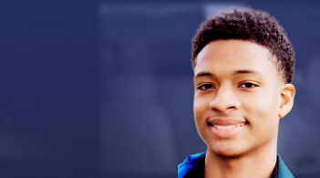 Smiling young man with short hair, wearing a blue jacket, against a blurred background.