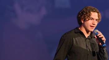 Young man speaking into a microphone on stage, showcasing confidence during a presentation at an event.