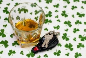 Image of car keys next to a glass of whiskey on a background of shamrocks