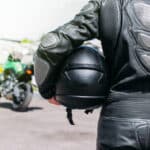 Image of someone in motorcycle leathers holding a motorcycle helmet