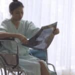 Image of a woman in a wheelchair and hospital gown looking at an x-ray