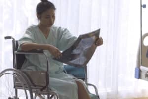 Image of a woman in a wheelchair and hospital gown looking at an x-ray