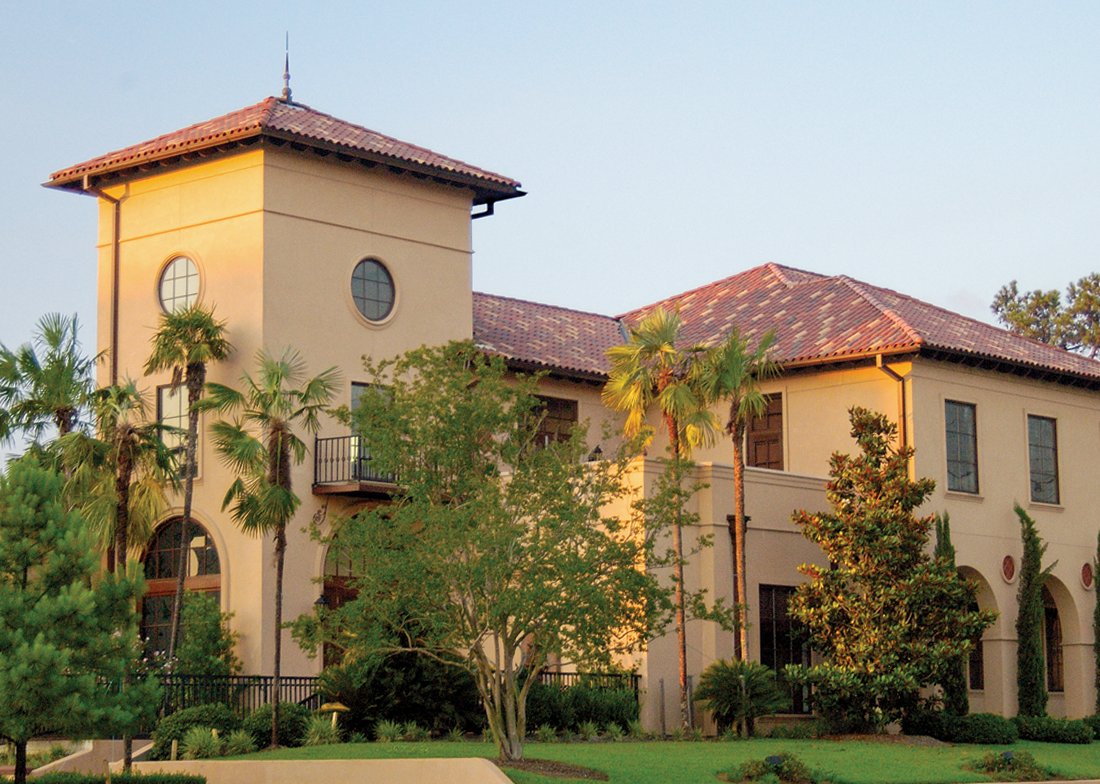 Mediterranean-style building with red-tiled roof, palm trees, and arched windows, bathed in warm sunlight.